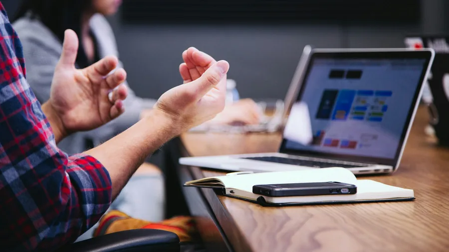 Hands explaining a point across a desk beside a laptop