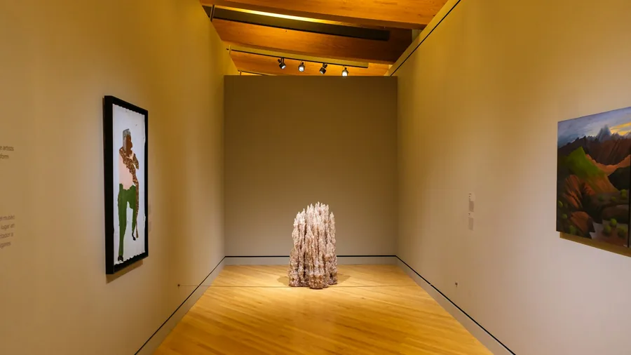 A gallery room hung with artworks around a sculpture